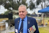A photo of a man looking at the camera with medals on his suit jacket 