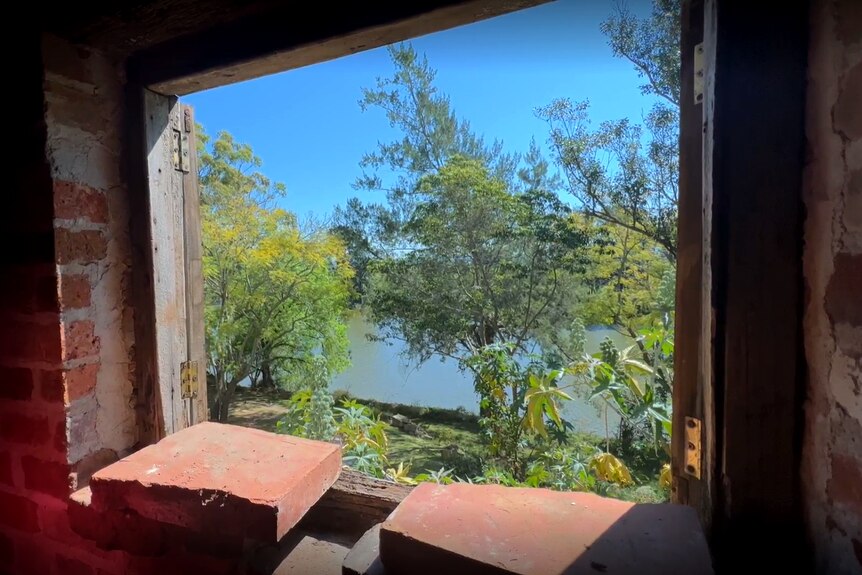 The view out a brick window, looking onto a river with a tree-lined bank.