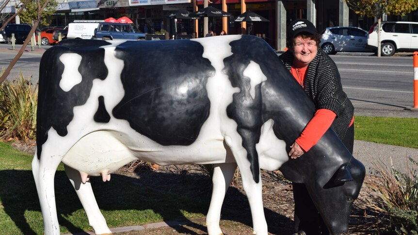 A lady wrapping her arms around the next of a fake dairy cow