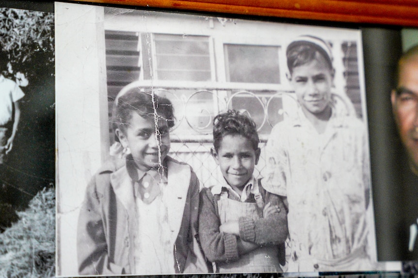 An old black and white photograph of three children standing next to each other smiling, sun on their faces.