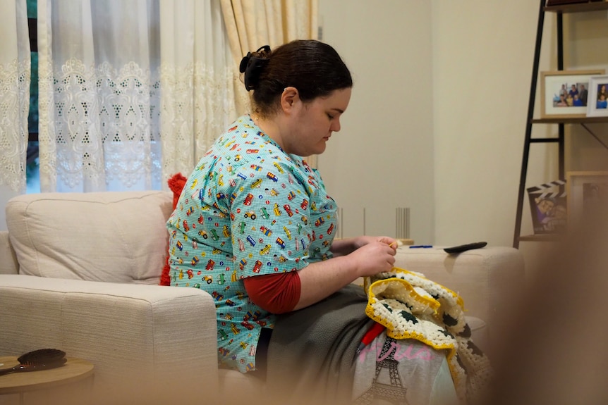 Stephanie Bell sits on a couch knitting a blanket