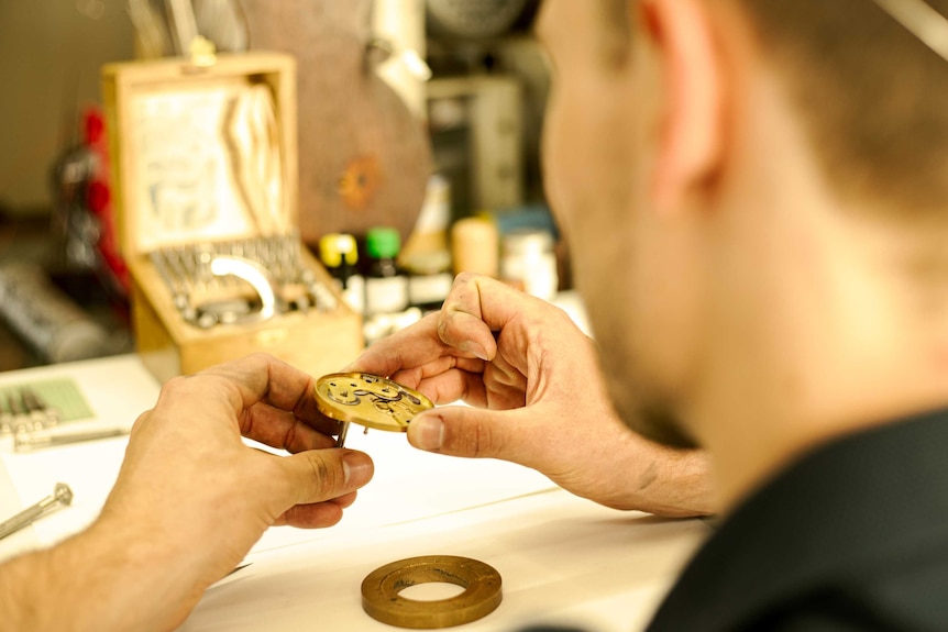 Dirty hands hold a finely crafted brass timepiece.