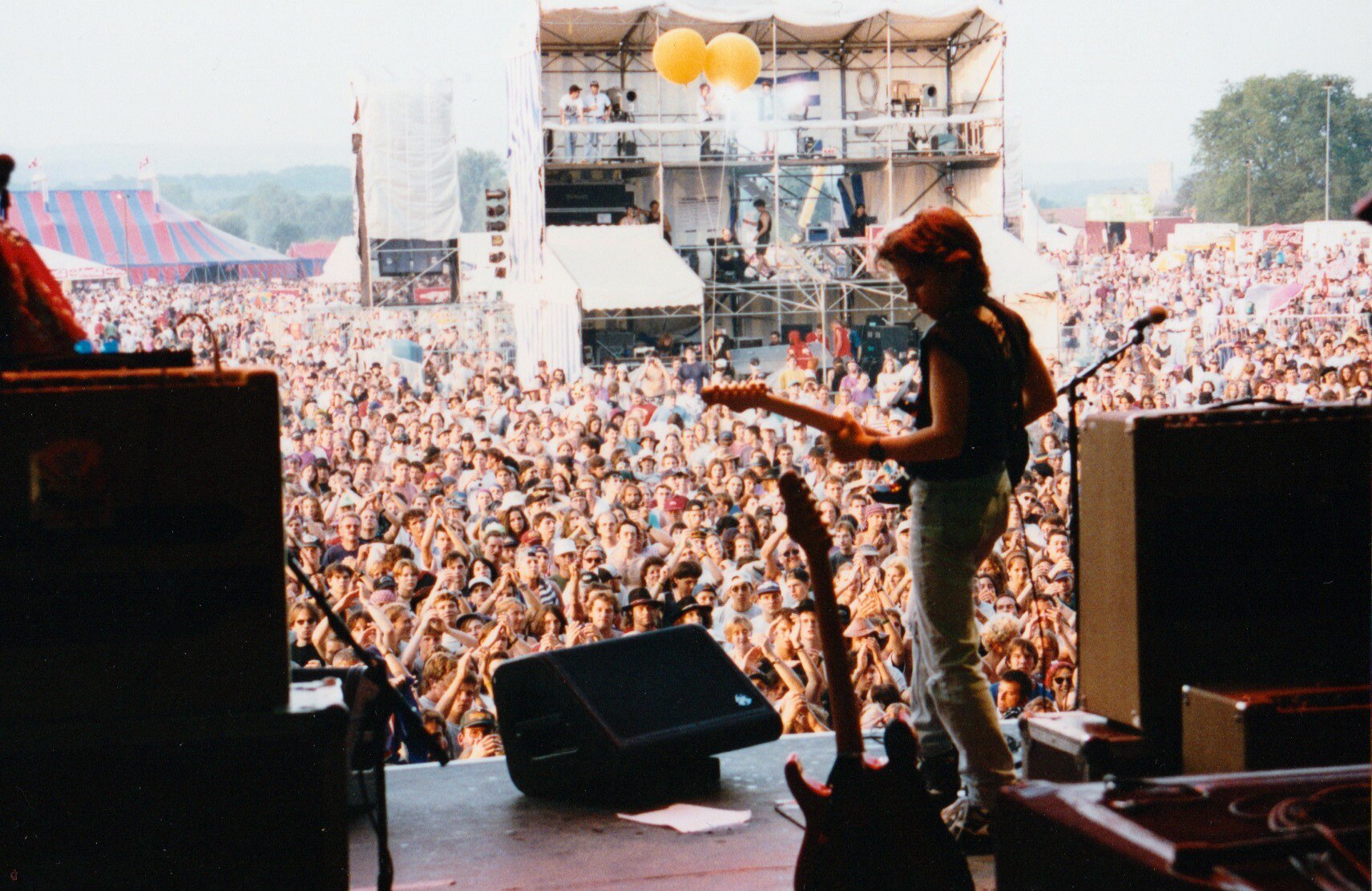 A teenage boy on stage holding a guitar in front of a large festival crowd