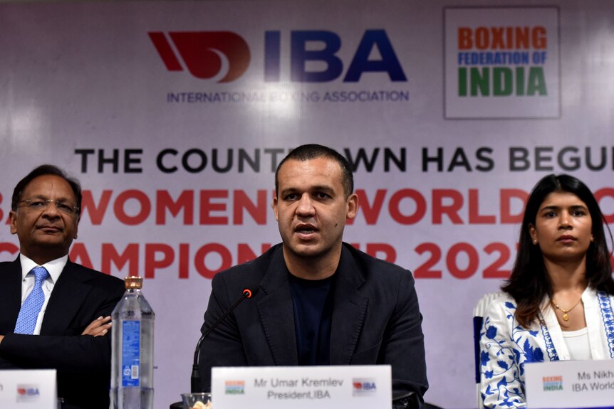 A boxing executive talks into a microphone at press conference in front of a sign "IBA Women's World Boxing Championship 2023".