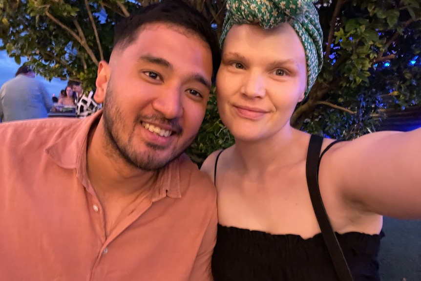 a selfie with a woman in a head scarf and man smiling into the camera at night