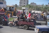 Palestinians drive down a road on motorbikes, cars, tractors and utility trucks