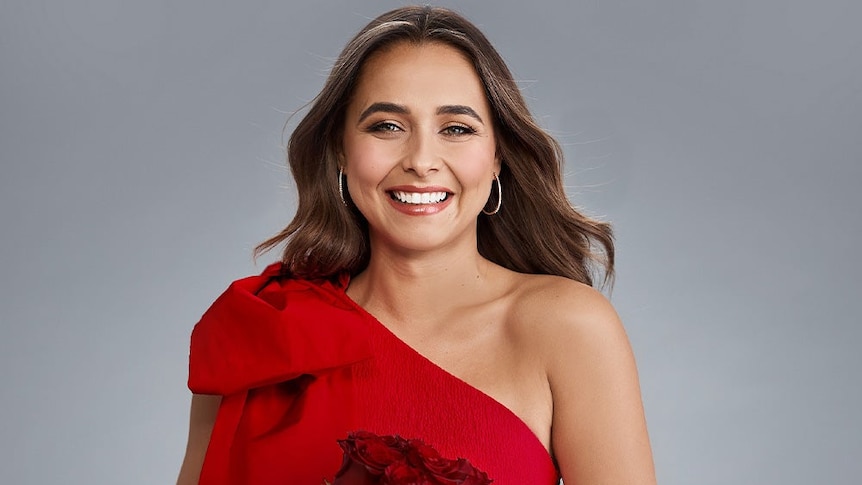 A wona in a red dress holding roses smiles directly at the camera.