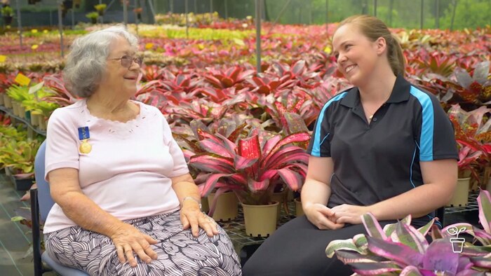 Two ladies smiling at each other with colourful plants in the background