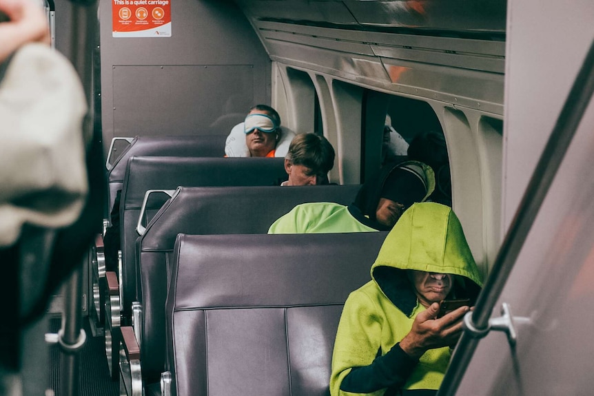 Tradie commuters sleeping and playing on their phone on a dawn train