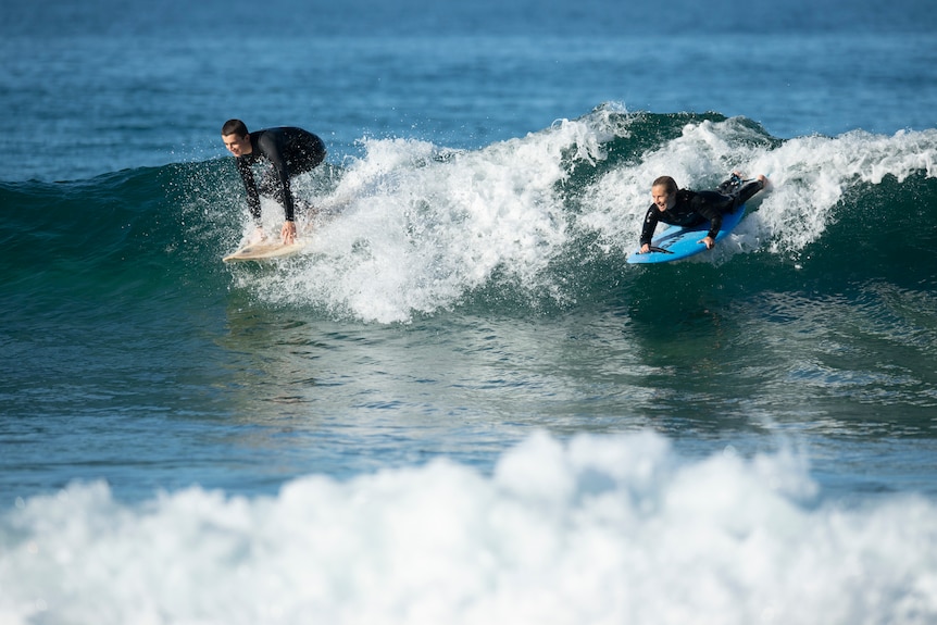 An Australian female para surfer lying on her surf board while catching a wave.