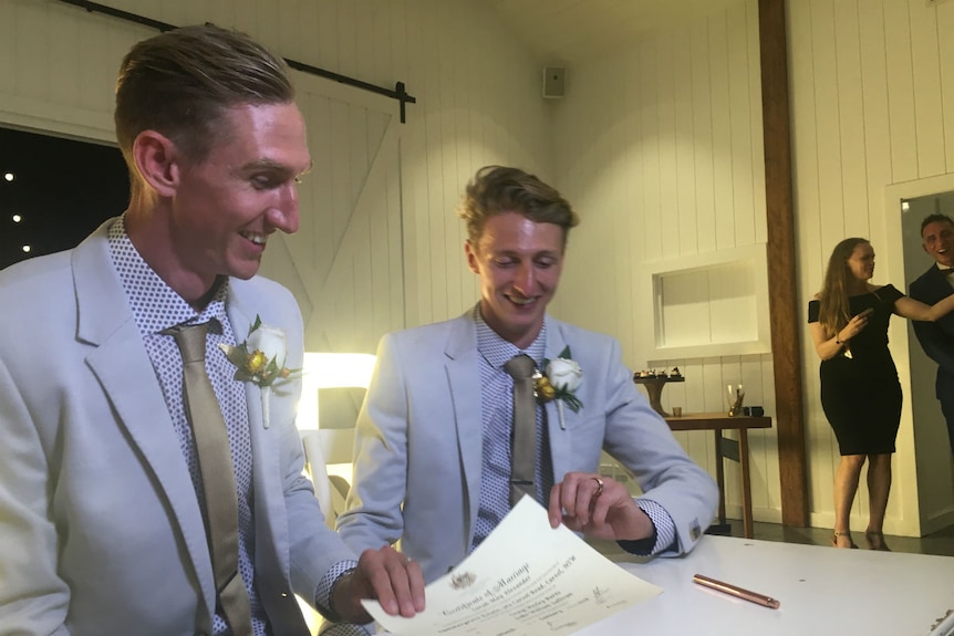 Craig Burns and Luke Sullivan smile as they sign their wedding certificate.