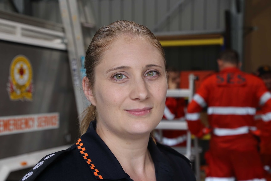 Eleanor Rosam smiles and looks into the camera as she stands in front of an SES crew member in a grey room.