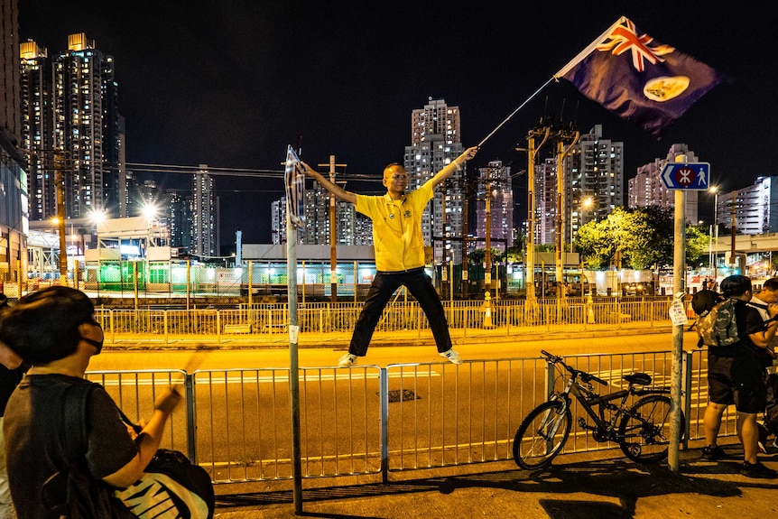 A protestor stands on railing by a road waving a flag.