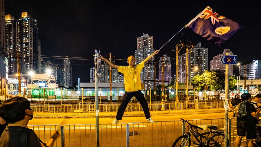 A protestor stands on railing by a road waving a flag.
