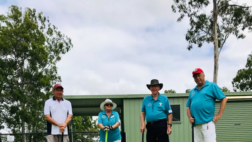 three croquet players standing behind a croquet ball and arch