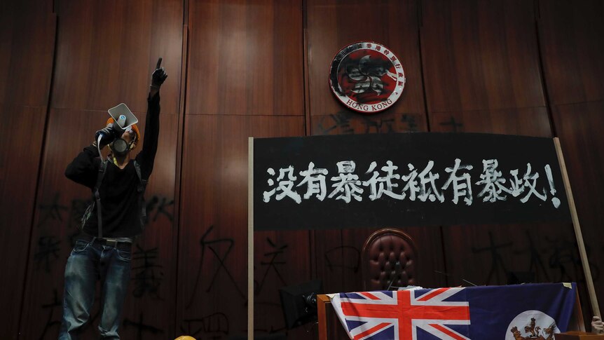 A protester shouts next to a defaced Hong Kong emblem and a banner which reads "No thug, only tyranny".