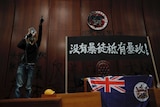 A protester shouts next to a defaced Hong Kong emblem and a banner which reads "No thug, only tyranny".