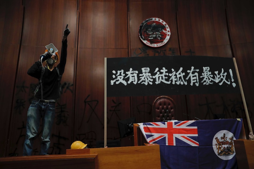 A protester shouts next to a defaced Hong Kong emblem and a banner which reads "No thug, only tyranny".