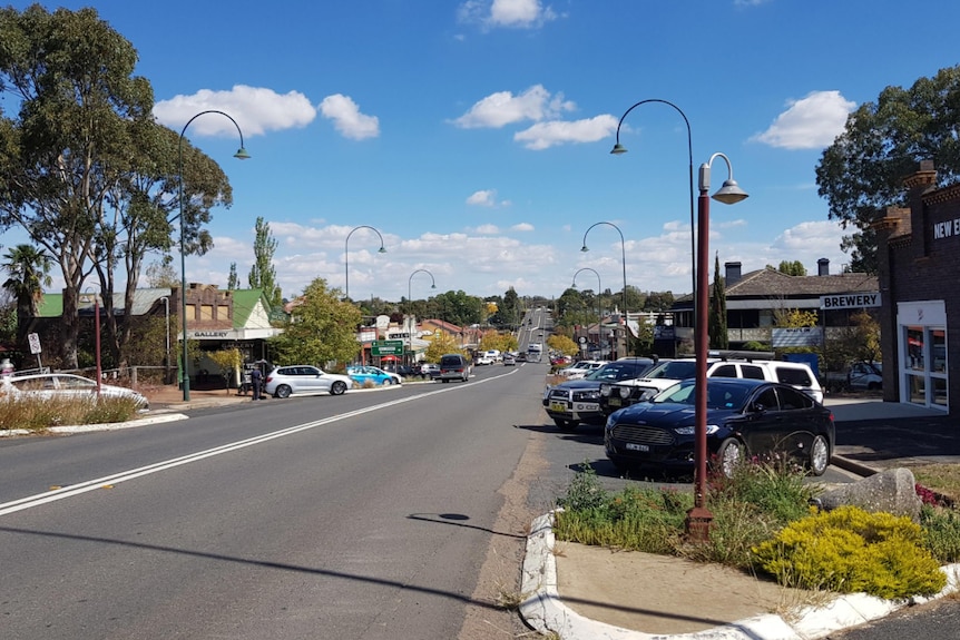 Main street of Uralla, town in NSW New England region, curved street lights, lined with cars and shops, bright cloudy day.