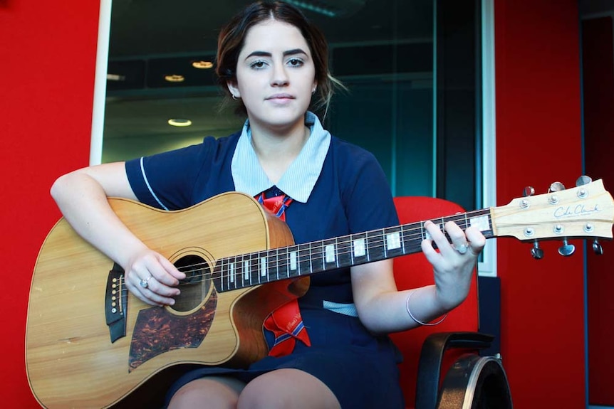 Tia sitting in ABC Tropical North studio with her guitar.