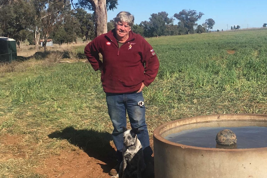 A man stands with a dog next to a water tank.