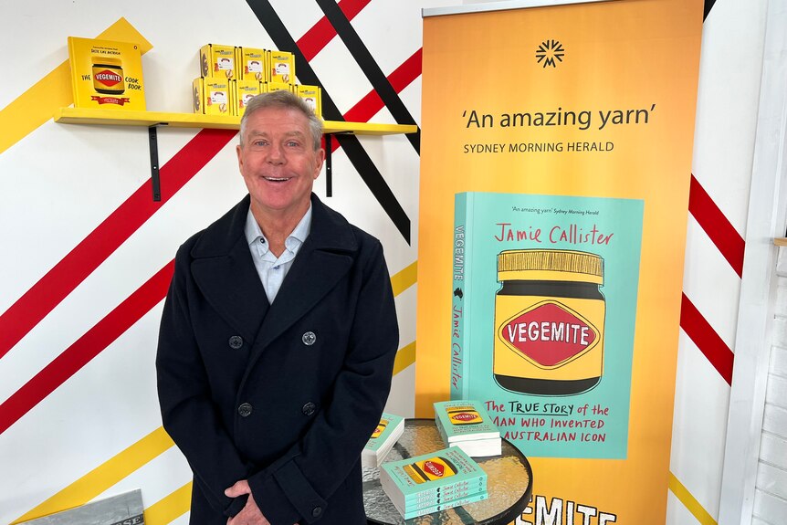 A man smiles in front of a vegemite banner