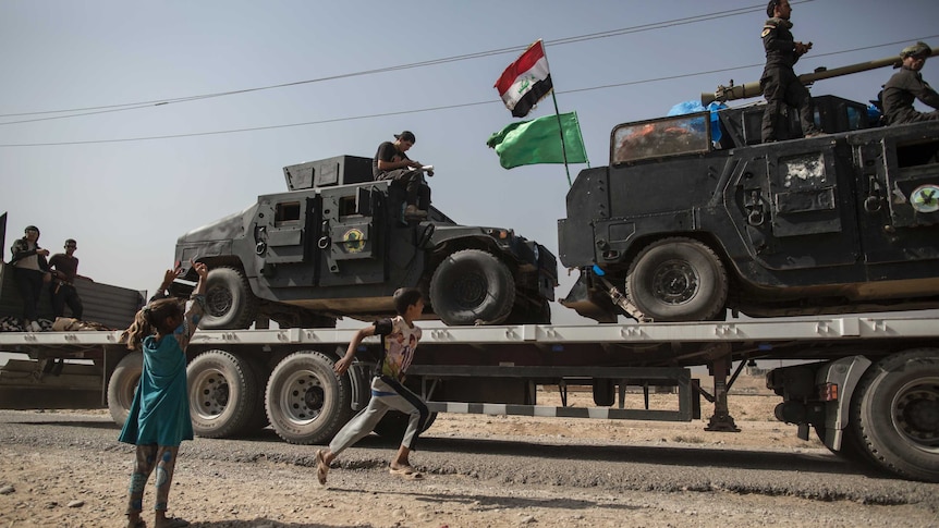 Children run beside military vehicles passing by in the village of Imam Gharbi, some 70km south of Mosul, Iraq.