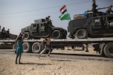 Children run beside military vehicles passing by in the village of Imam Gharbi, some 70km south of Mosul, Iraq.