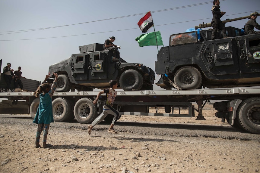 Children run beside military vehicles passing by in the village of Imam Gharbi, some 70km south of Mosul, Iraq.