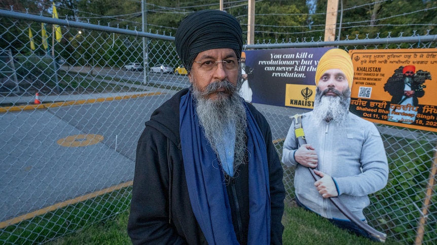 Behind Gurmeet Singh Toor is a yellow circle on a driveway behind a fence, which has a picture of Hardeep Singh Nijjar on it
