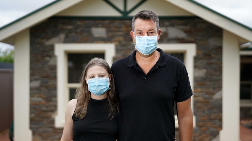 A woman and a man wearing face masks outside a house