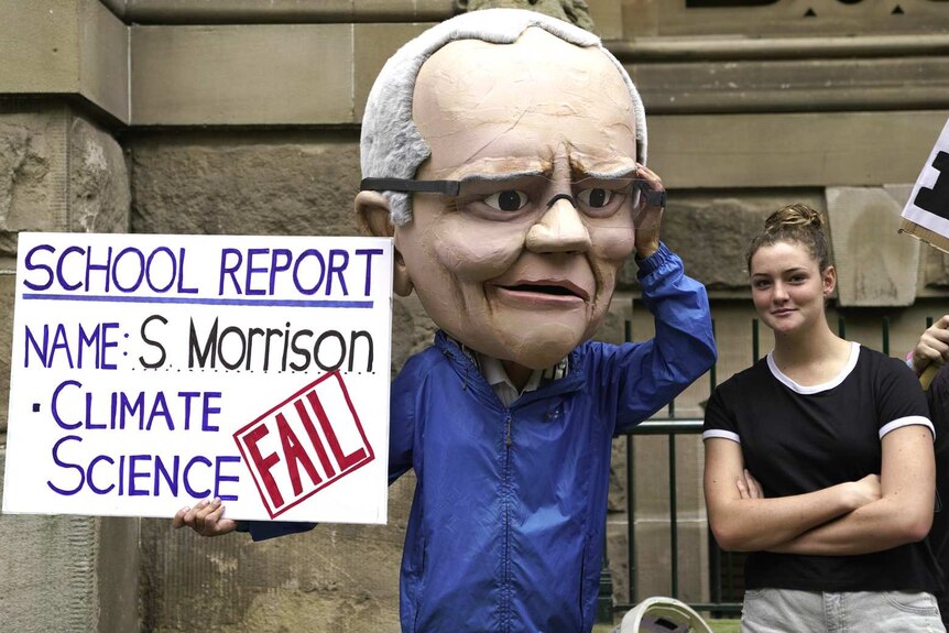 person in scott morrison paper mache head with protest sign