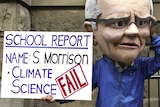 person in scott morrison paper mache head with protest sign