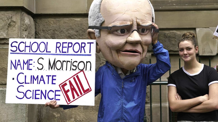 person in scott morrison paper mache head with protest sign