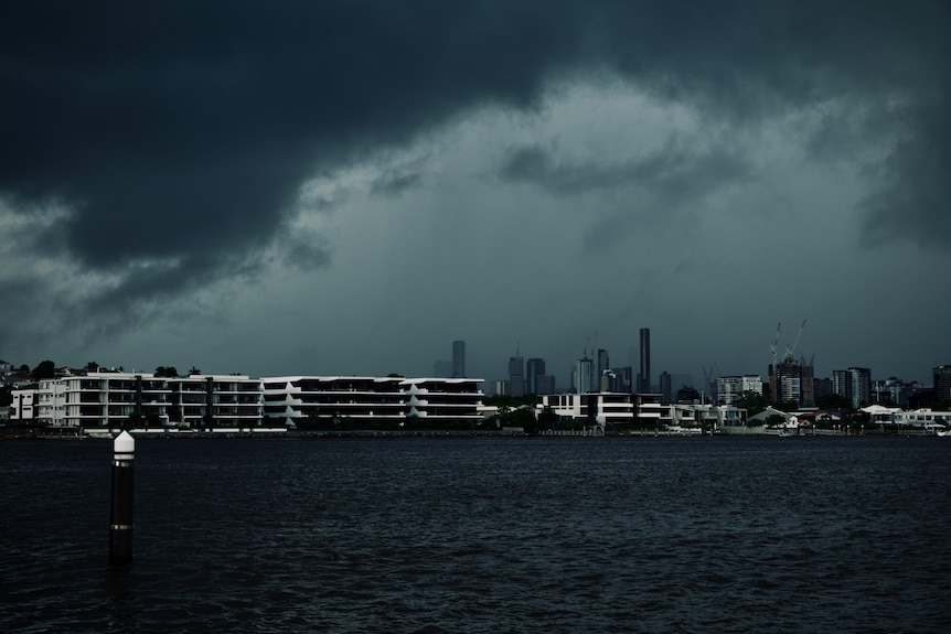 Dark storm clouds over Brisbane river with city in background.