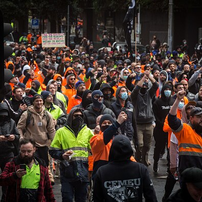 Hundreds of men in hi-vis clothing march down a street holding signs