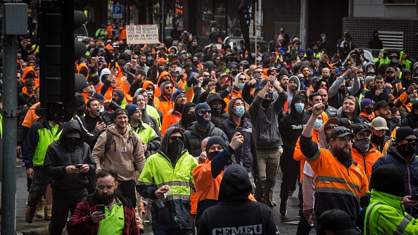 Hundreds of men in hi-vis clothing march down a street holding signs