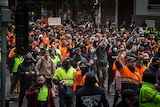 Hundreds of men in hi-vis clothing march down a street holding signs