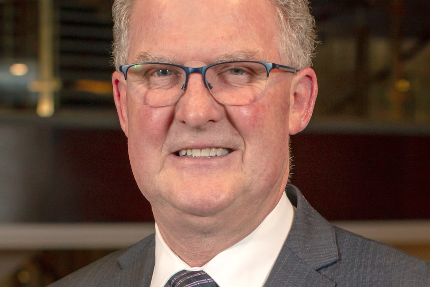 headshot of a man wearing glasses and a grey suit