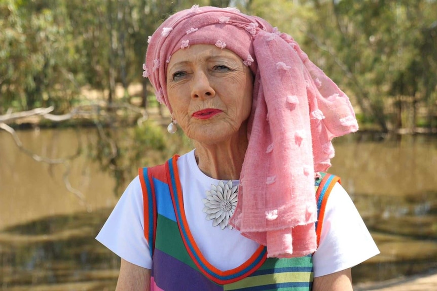 A woman with a headdress and colorful clothes looks forward.