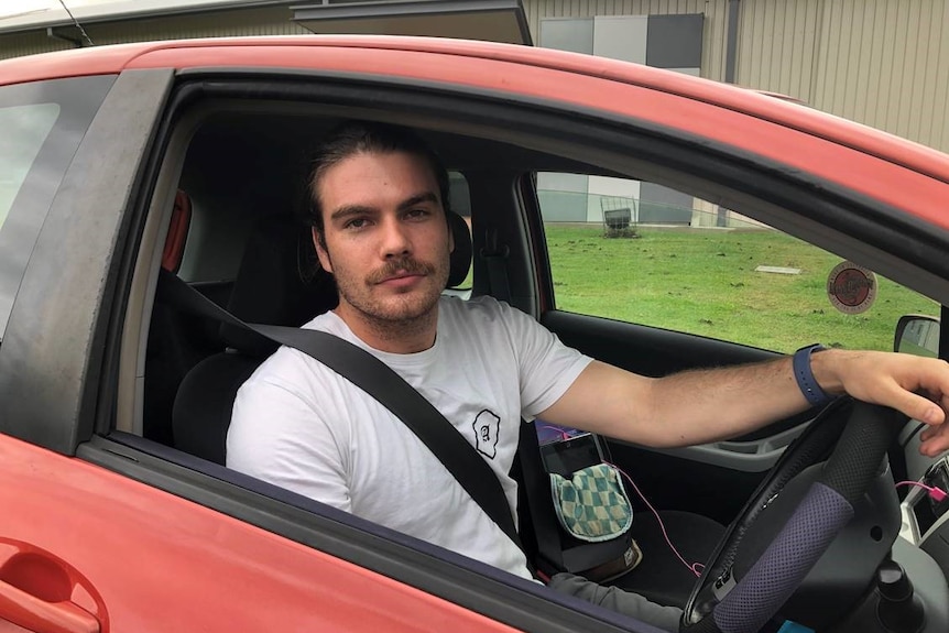 A young man sits in the driver's seat of a red car