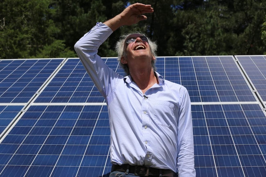 Keith Bladon looks to the sky with his solar panels behind him.