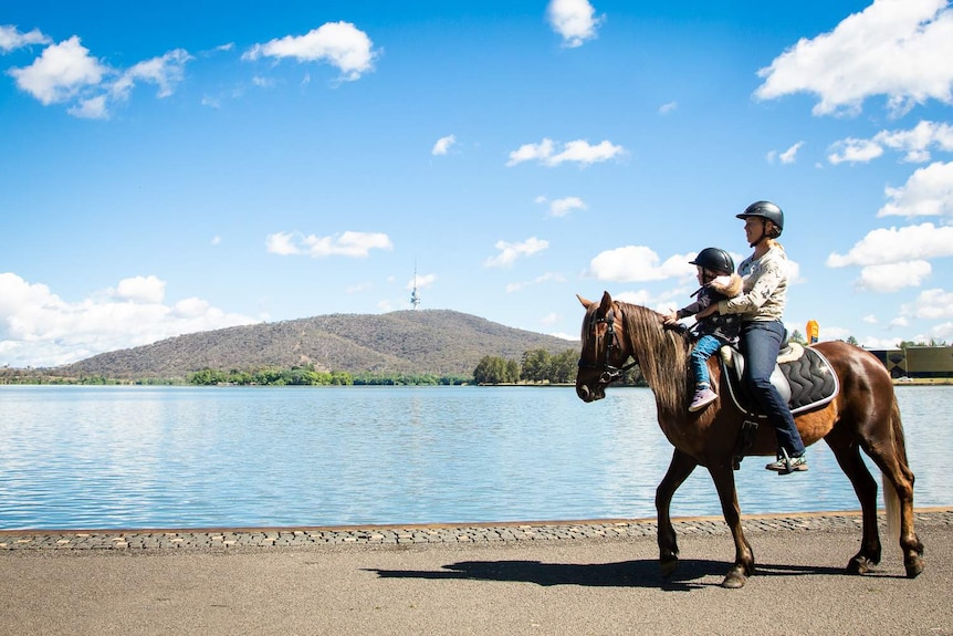 Lauren Woodbridge is riding her brumby along a path by Lake Burley Griffin.