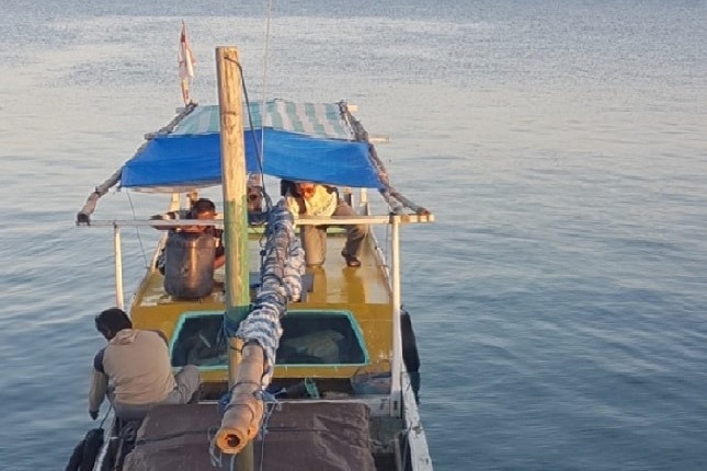 A wooden fishing boat with sails rolled up motors out on blue water