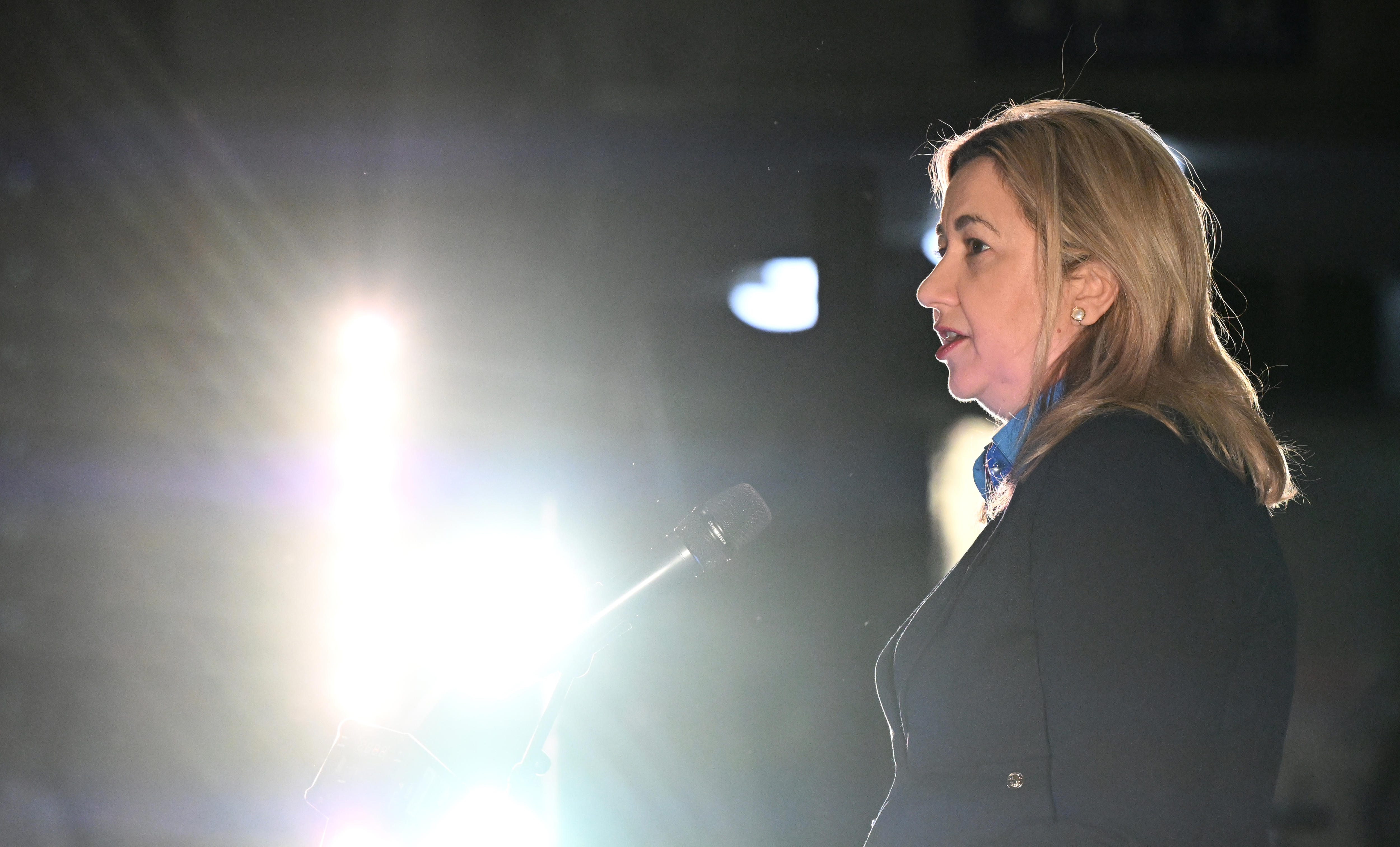 premier annastacia palaszczuk at a vigil at night speaking into a microphone, a bright light is shining beside her