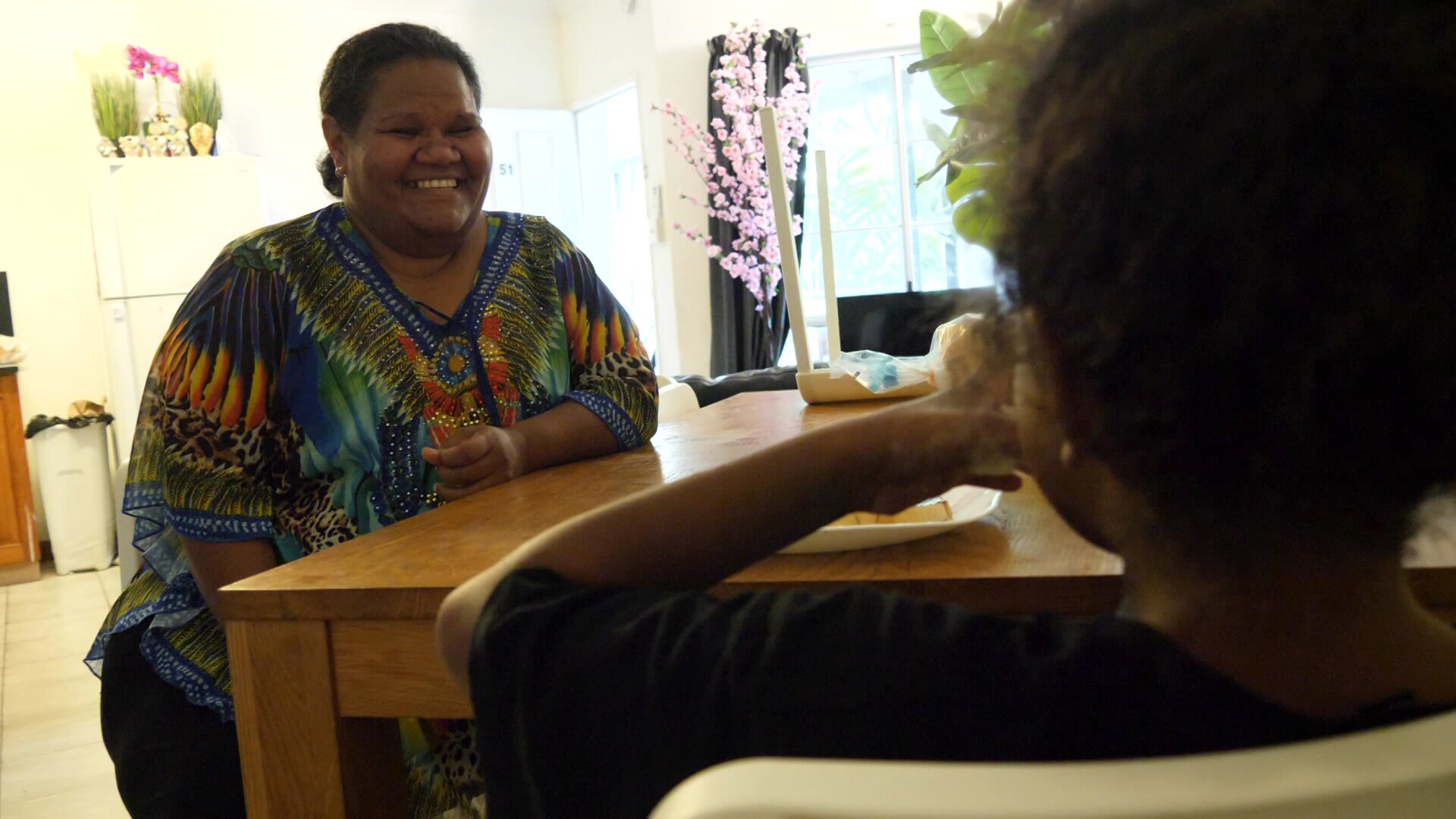 Mujer sonriendo mientras su pequeña hija le da un mordisco a un sándwich. 