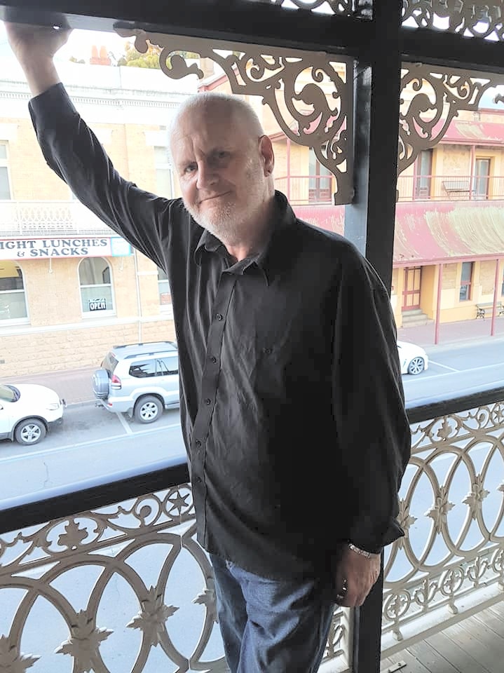 Rennie stands on a hotel verandah smiling.