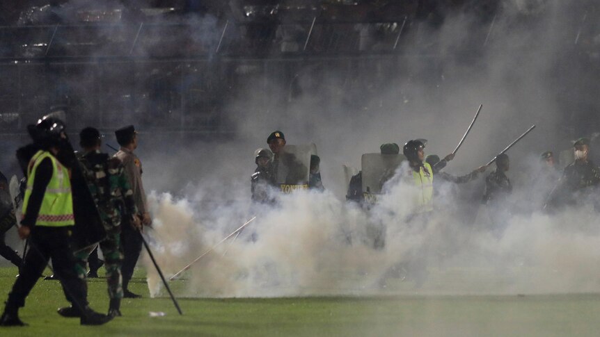 Police officers and soldiers stand on a football pitch amid tear gas smoke.