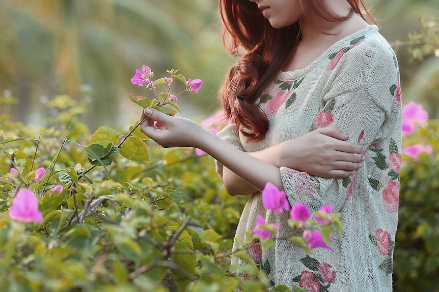 Woman looking sad in a garden holding a flower