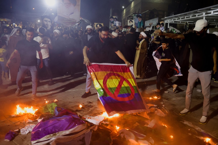 Man holding rainbow flag with cross on it holds flag to flames 